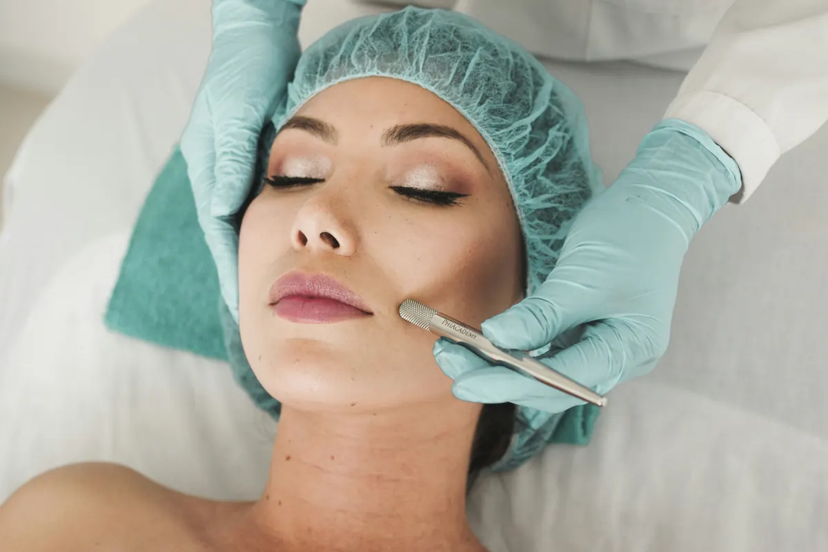 Client lying on a treatment bed while a gloved practitioner performs a facial skin treatment