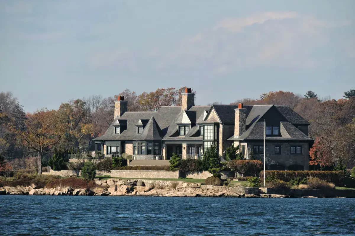 Large waterfront house with gabled roofs and stone chimneys on the Greenwich, Connecticut shoreline in autumn