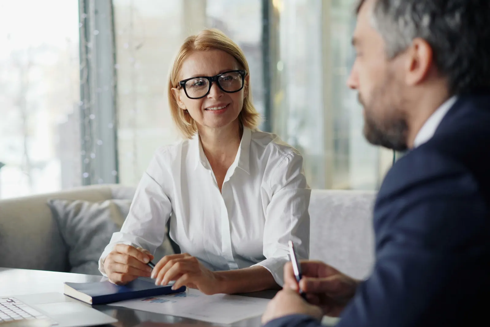 Smiling woman in glasses meeting with a man in a navy suit at a table in a bright office