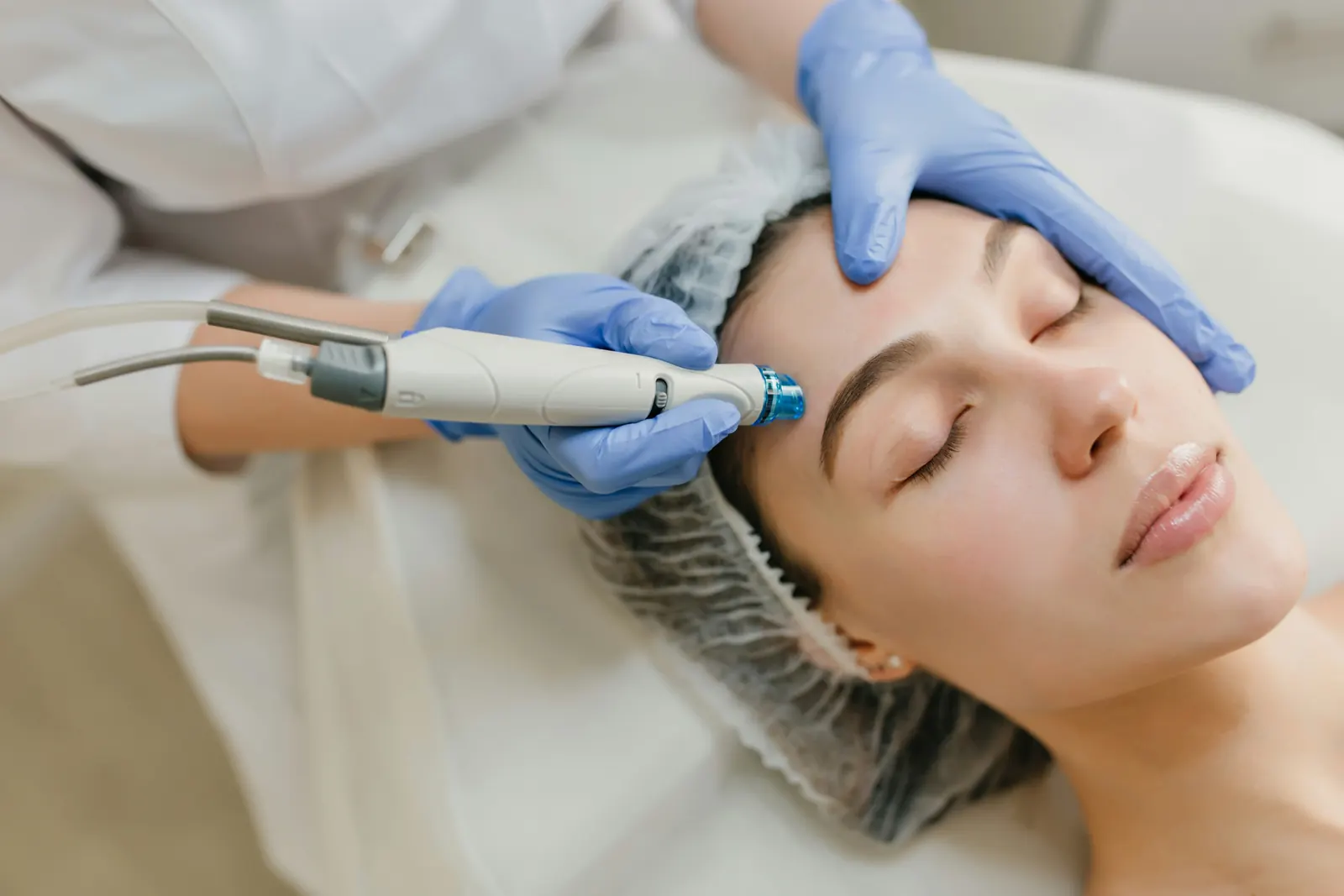 Aesthetic practitioner in blue gloves using a handheld skin-treatment device on a client's forehead