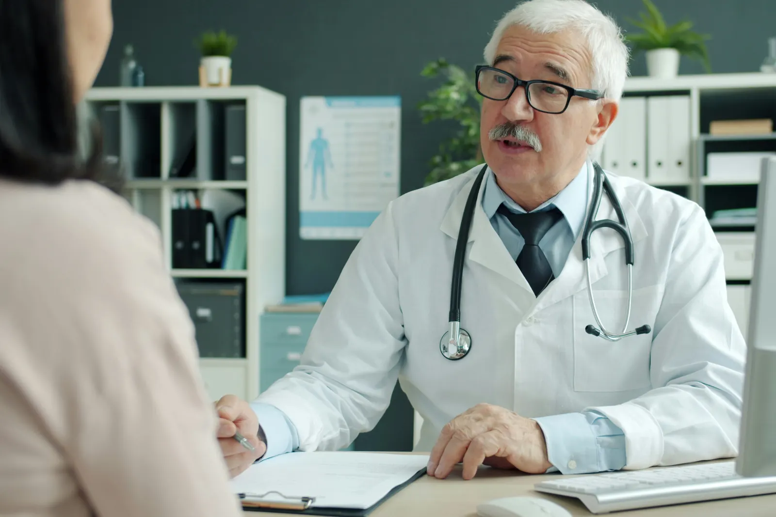 Physician in a white coat talking with a patient across his desk during an office consultation