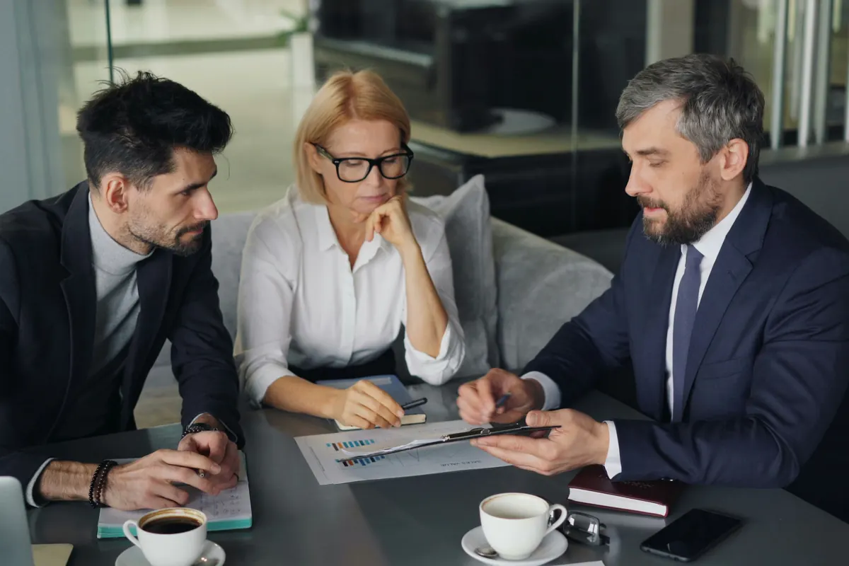 Three professionals reviewing documents together at a table with coffee cups